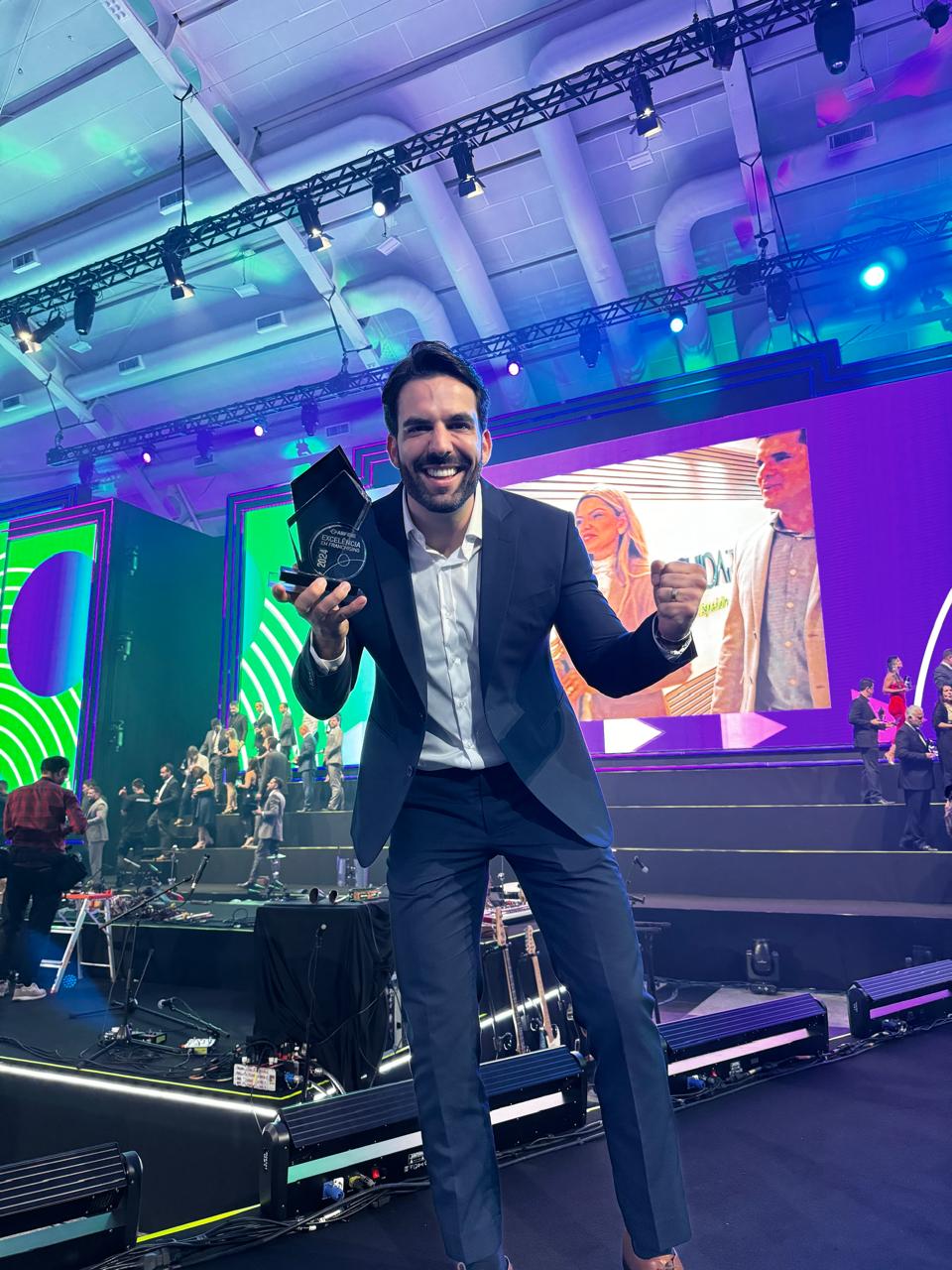 Daniel Neves sorrindo, segurando um troféu de reconhecimento em um evento do setor